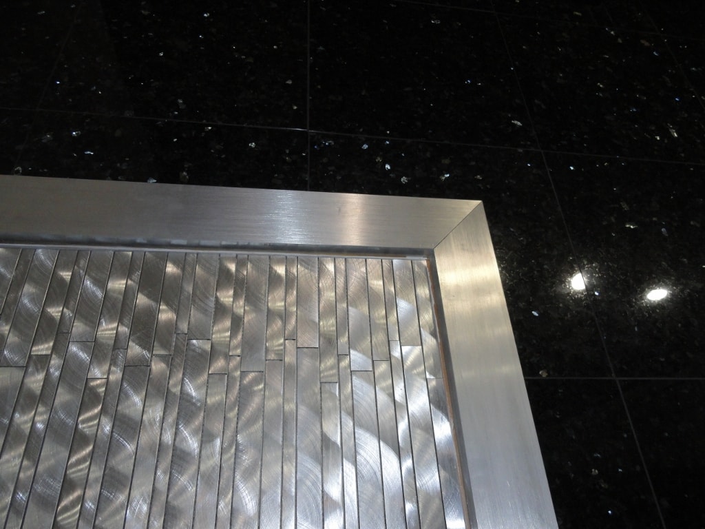 Brushed metal mosaic tile sample on black granite surface